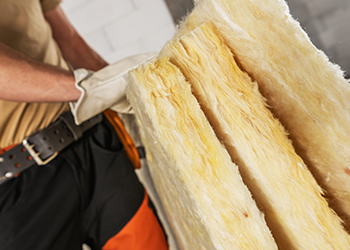 A construction worker wearing a tool belt is installing insulation in a wall.